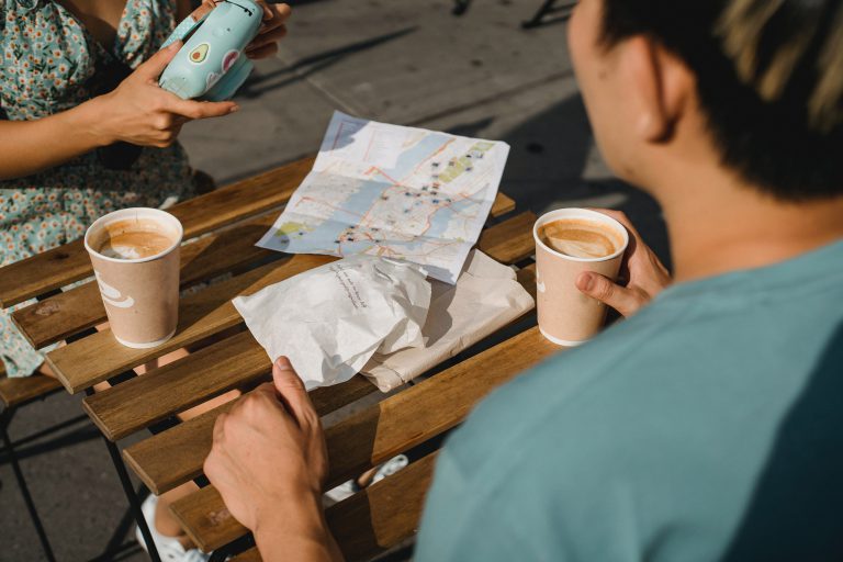 Two people drinking coffee together. There is a map laid out on the table.